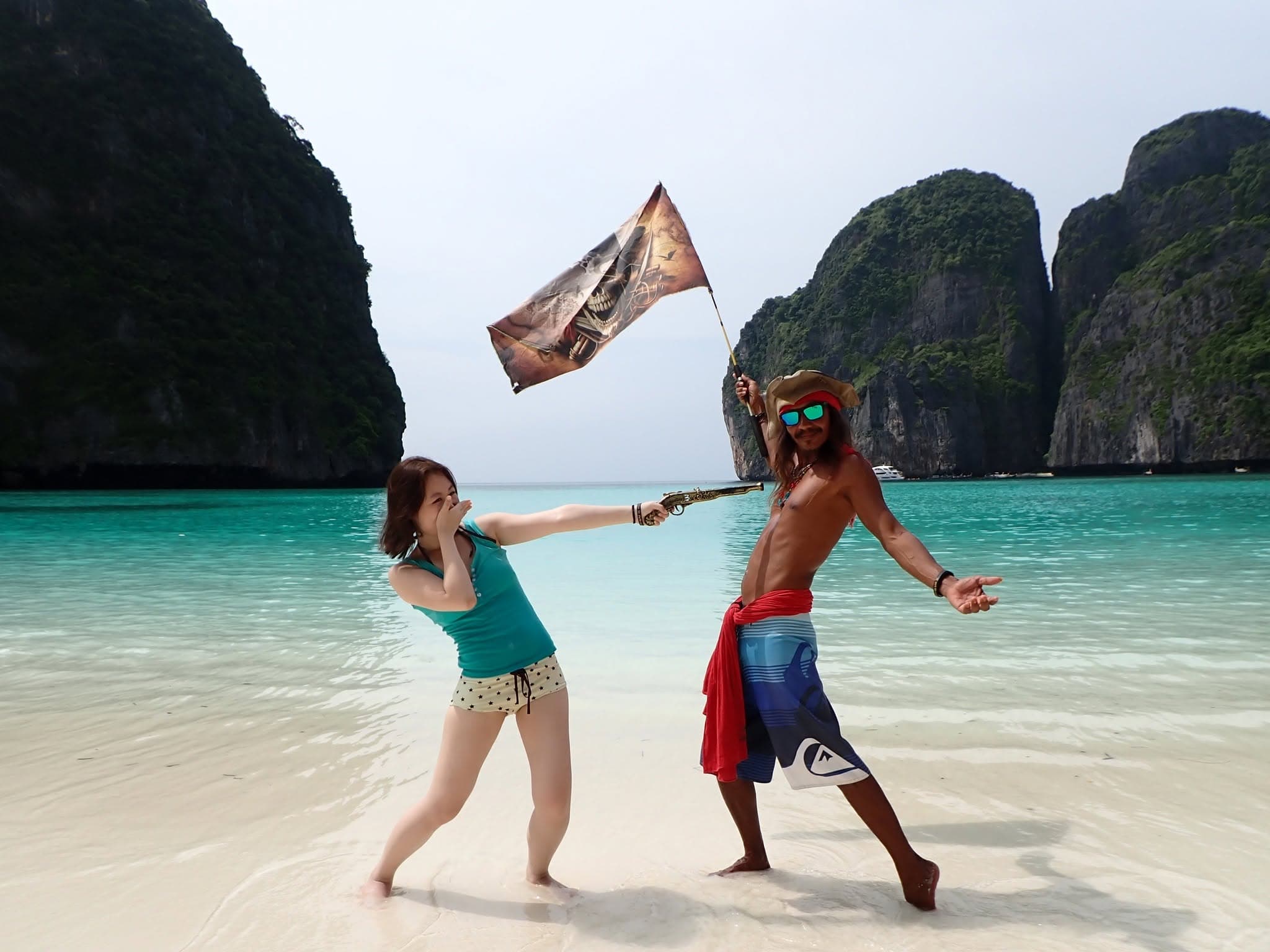 A guest and a pirate crew member with a pirate flag on the beach at Maya Bay